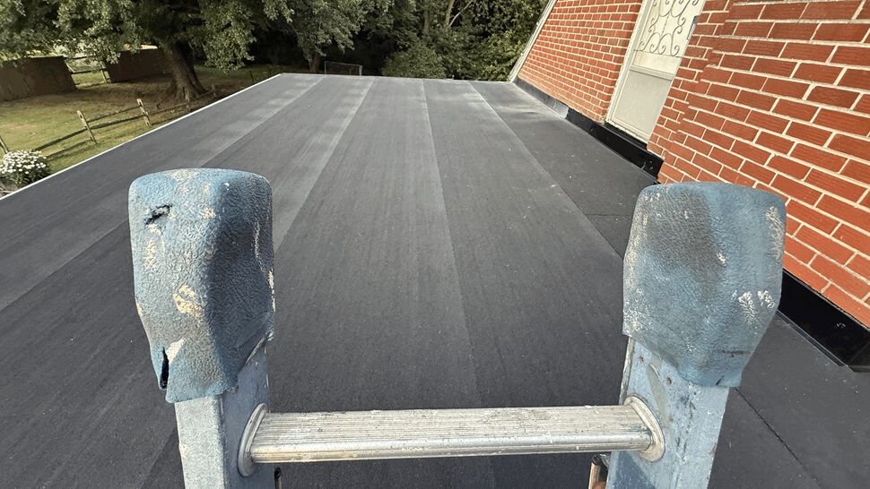Flat roof ladder close-up | Atlas Exteriors Close-up of ladder resting on smooth black flat roof surface.