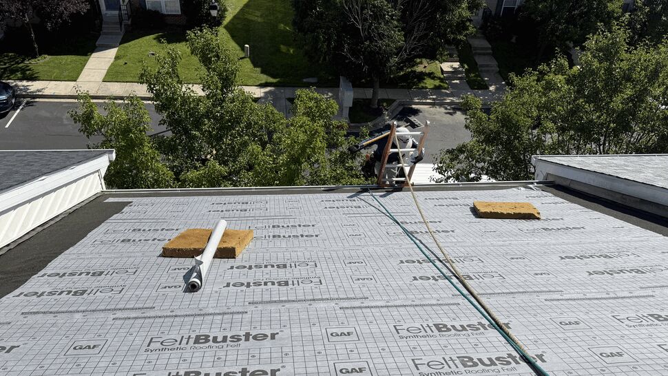 Flat roof covered in FeltBuster synthetic underlayment with vents and tools.