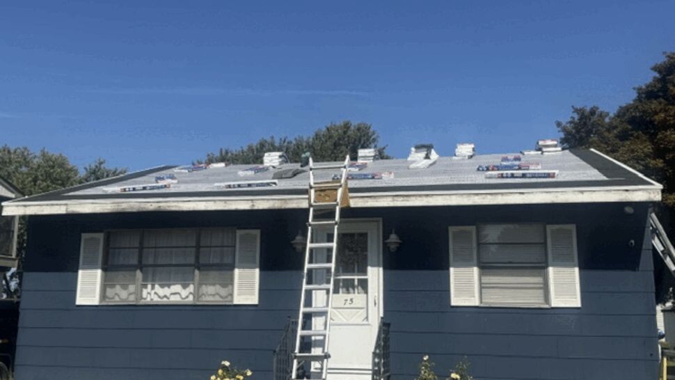 Front elevation of blue house with ladder to roof and materials on top