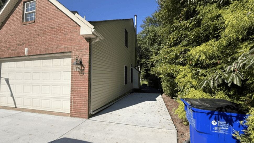 Garage side and driveway with visible gutters and a recycling bin