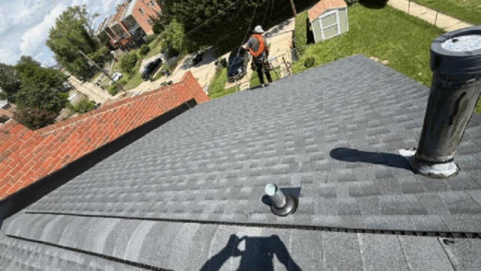 Gray asphalt shingle roof with vents | Atlas Exteriors Close-up of gray asphalt shingles with roof vents and a worker visible beyond the roofline.