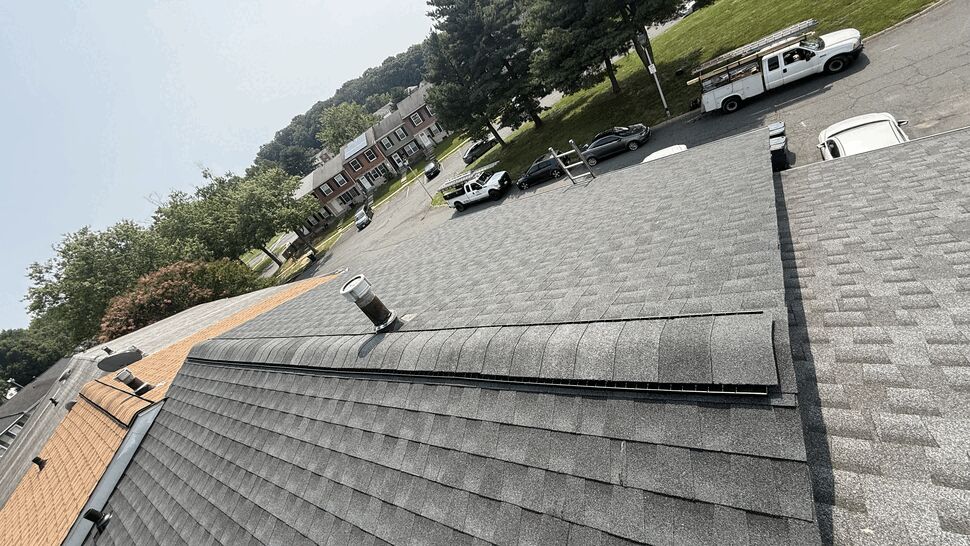 Aerial view of gray asphalt shingles with a ridge vent and plumbing vent pipe.