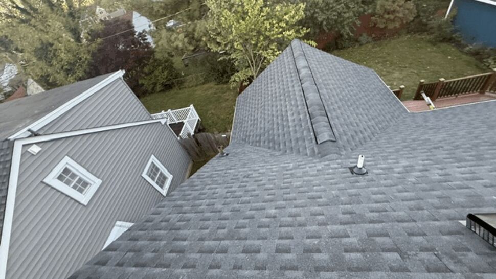 Aerial view of a gray shingle roof beside a gray-sided home.