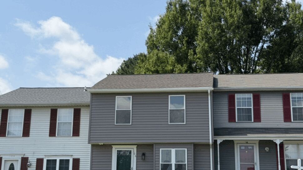 Front view of gray townhouse with vinyl siding and small shrubs.