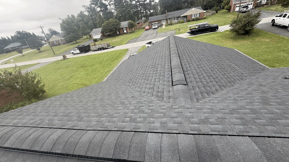 Aerial view of a grey shingle roof ridge over a residential street.