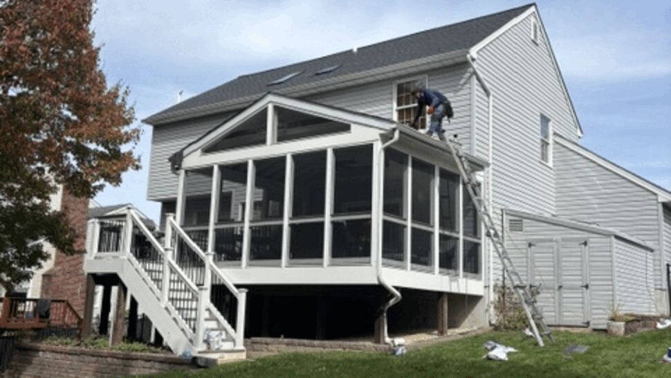 Worker performs roof and gutter work beside a screened porch.