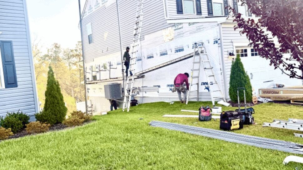 Home siding project with workers, tools, ladders, and materials on the lawn
