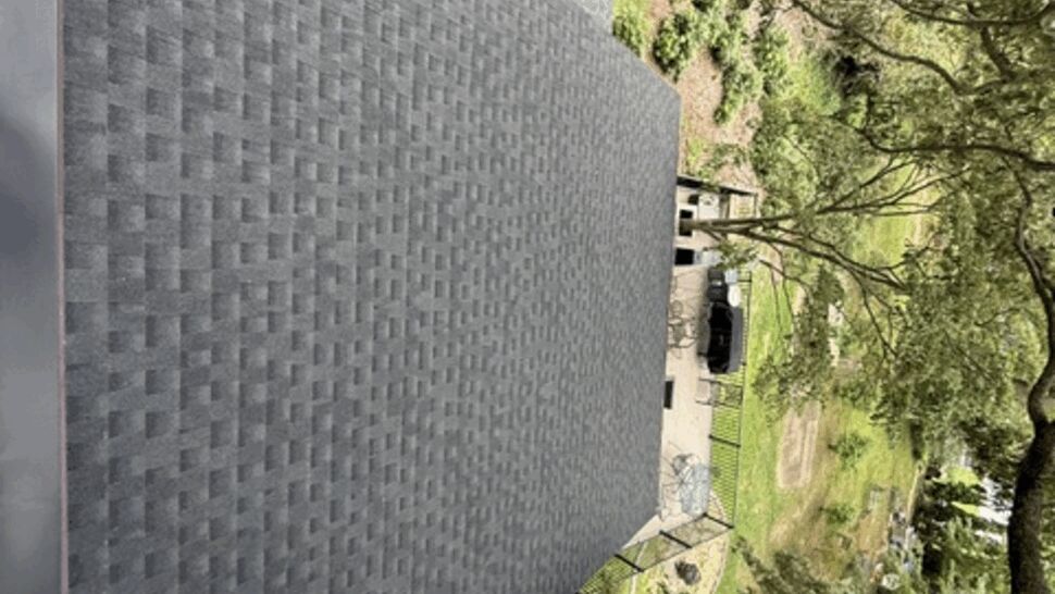 Top-down view of a long continuous gray shingled roof above a backyard patio.