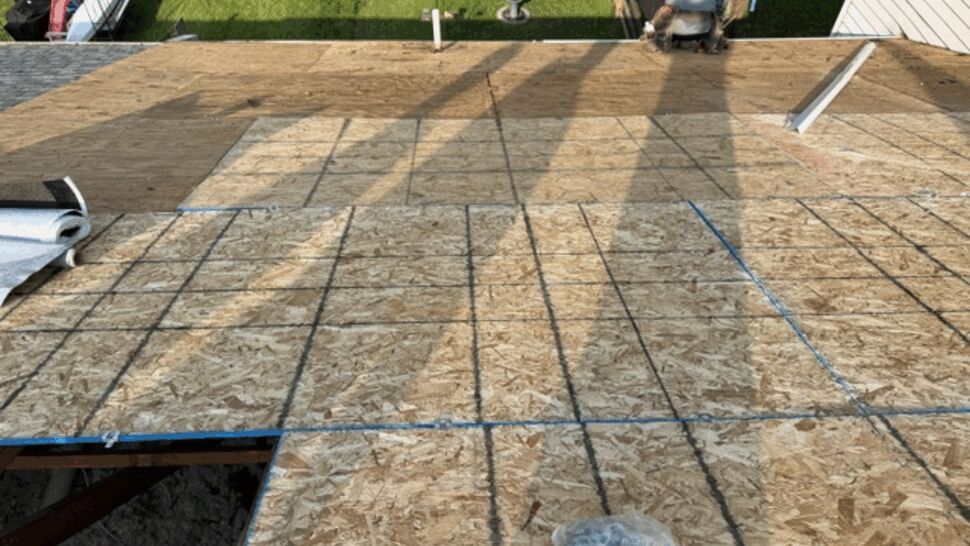 Close-up of OSB roof deck with chalk lines and rolled underlayment at edge.