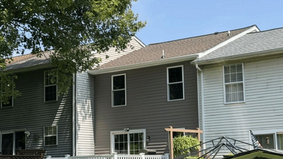 Rear view of rowhome with brown siding and a white deck under a clear sky.