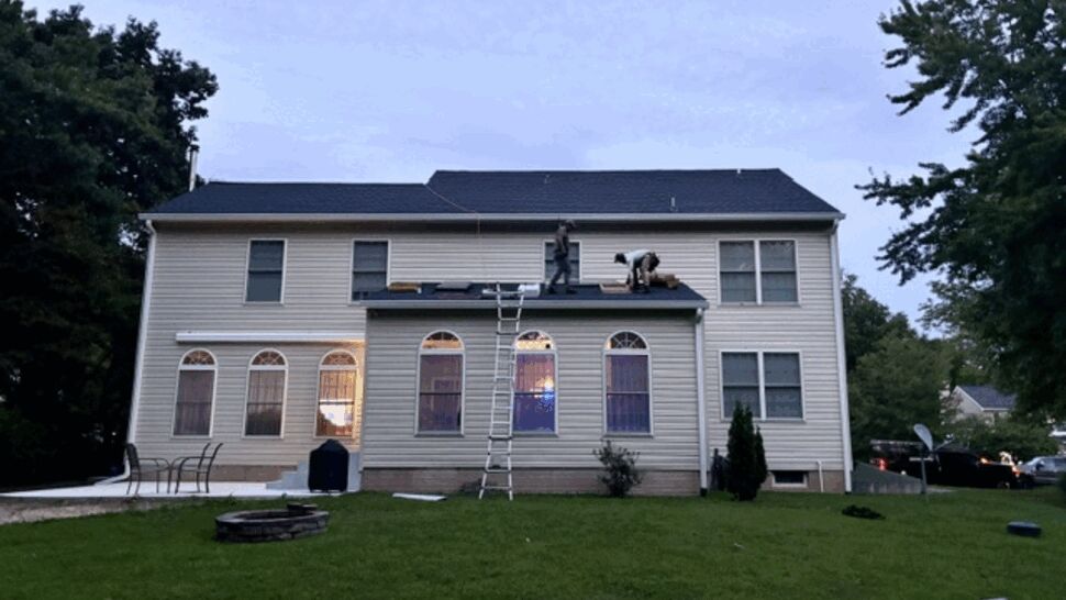 Back of house at dusk with workers on a lower roof and a ladder