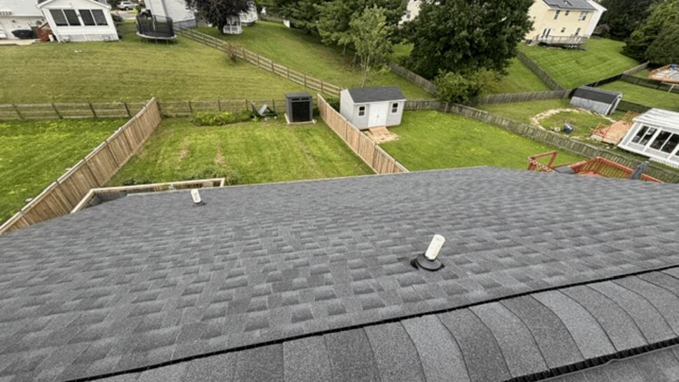 Backyard view from the roof showing new gray shingles and fenced yards.