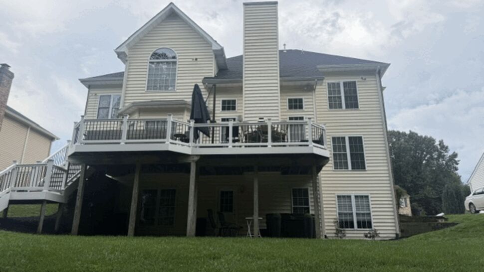 Rear of light-colored home with elevated deck and vinyl siding.
