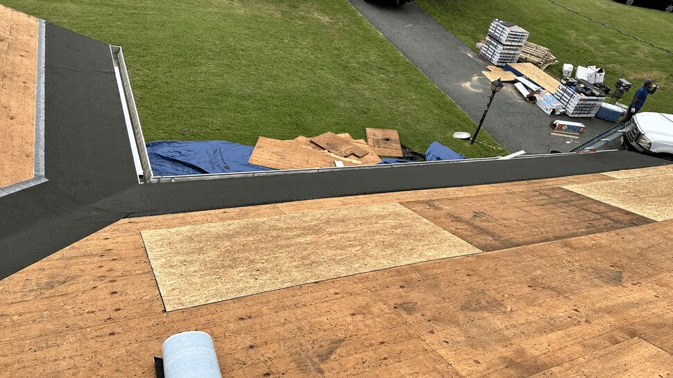 Roof deck with plywood and underlayment near a valley and materials on the ground.