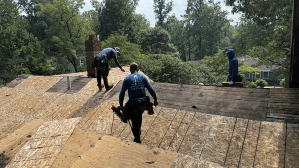 Three crew members walking on exposed plywood roof decking during tear-off.
