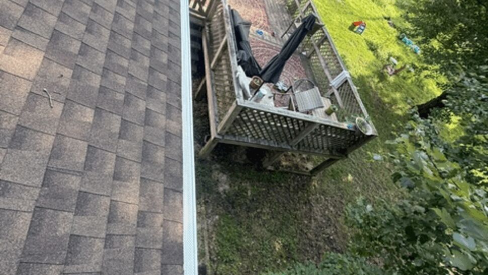 Aerial view along shingled roof edge with white gutter above backyard deck.