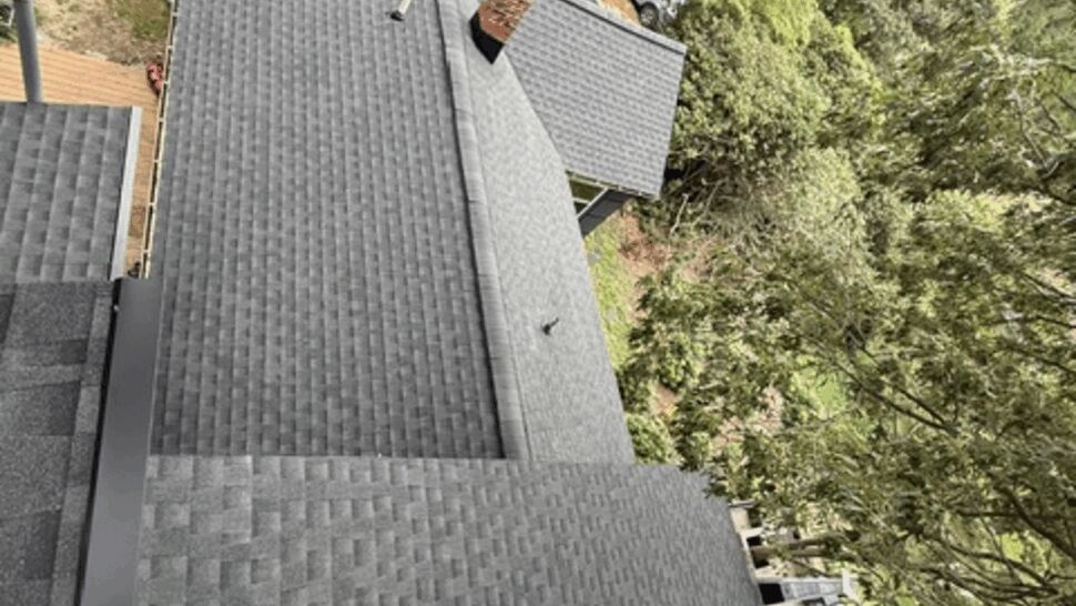 Top-down view of a newly shingled roof with work trucks and crew visible on the ground.