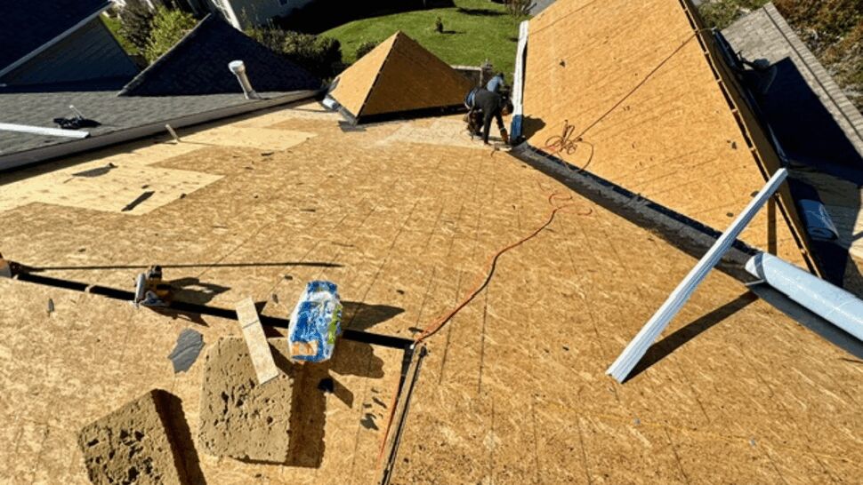 Roof replacement in progress with exposed plywood decking and workers
