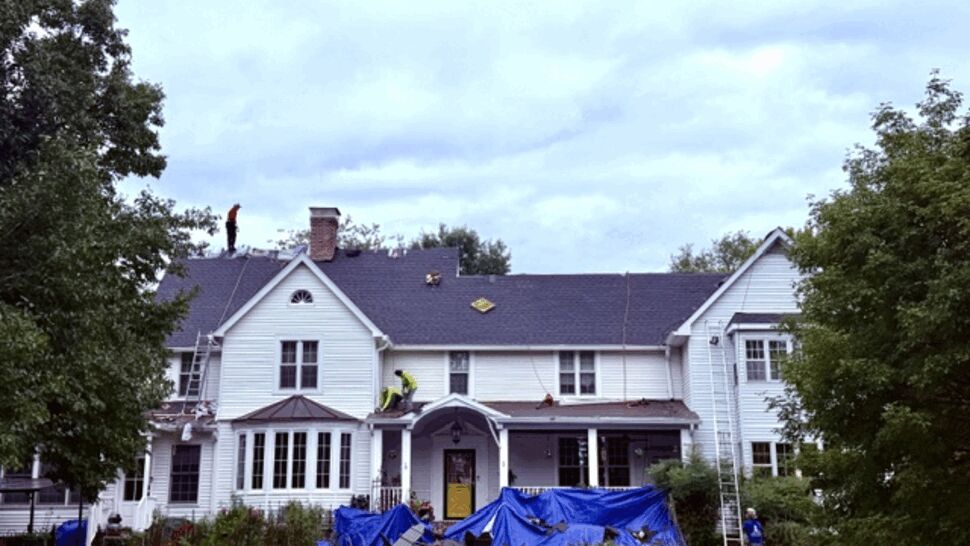 Roofing crew replacing shingles on a large white home