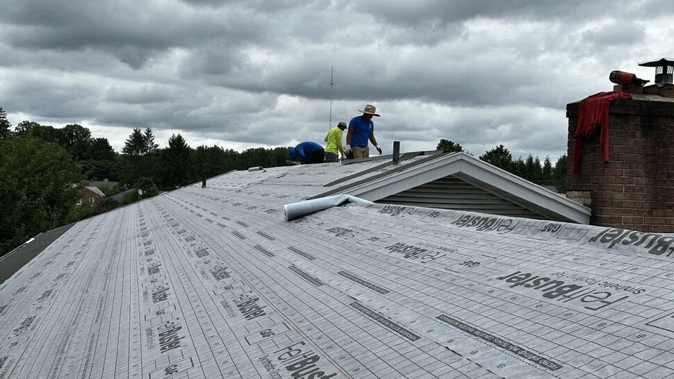Roofers installing underlayment on a residential roof beneath cloudy skies