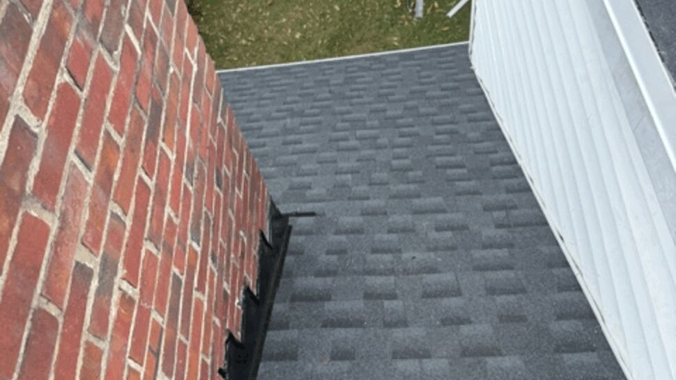 Gray shingle roof meeting a brick wall and light-colored siding.