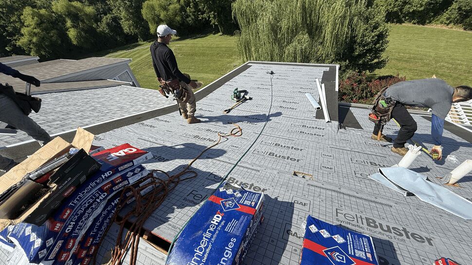 Roofers working on a roof with stacked GAF Timberline shingle bundles and tools.
