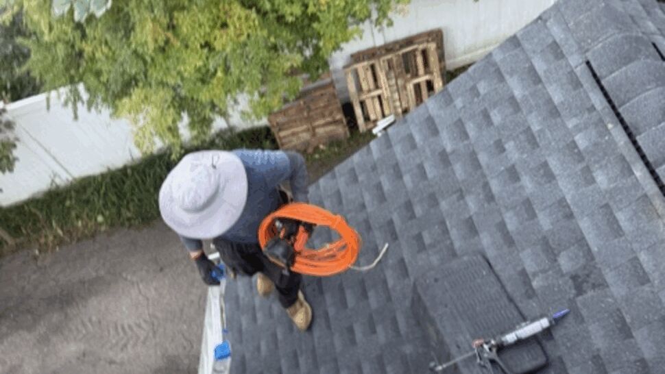 Two roofers wearing safety equipment work on a gray shingle roof.