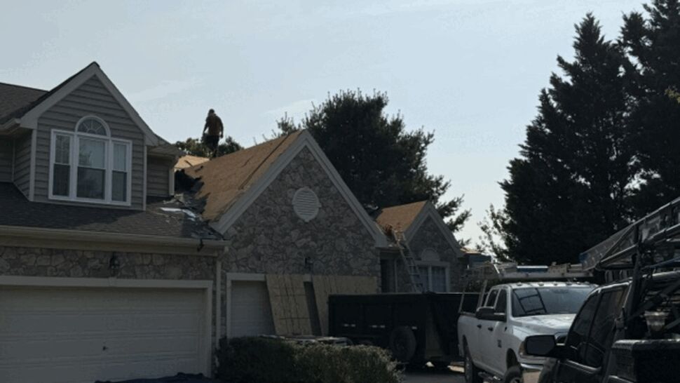 Jobsite view with roofing trucks, dumpster and crews at a tear-off project.