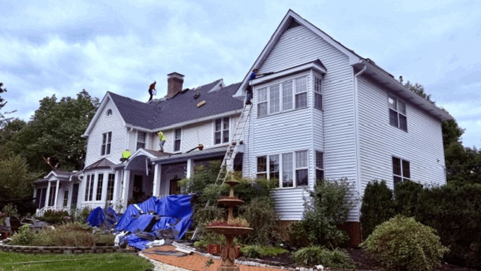Workers installing a roof on the side of a white home