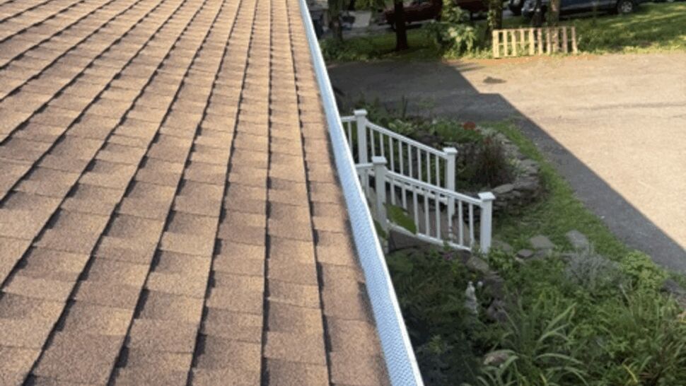 Long view along roof shingles and white gutter above the home's entrance and landscaping.