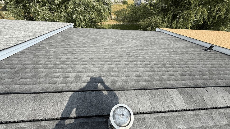 Rooftop image showing a plumbing vent and a worker shadow on new shingles.