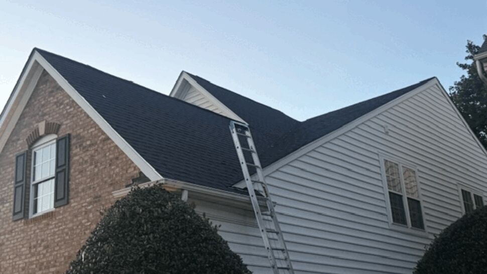 Ladder leaning against side gable roof with shingles removed.