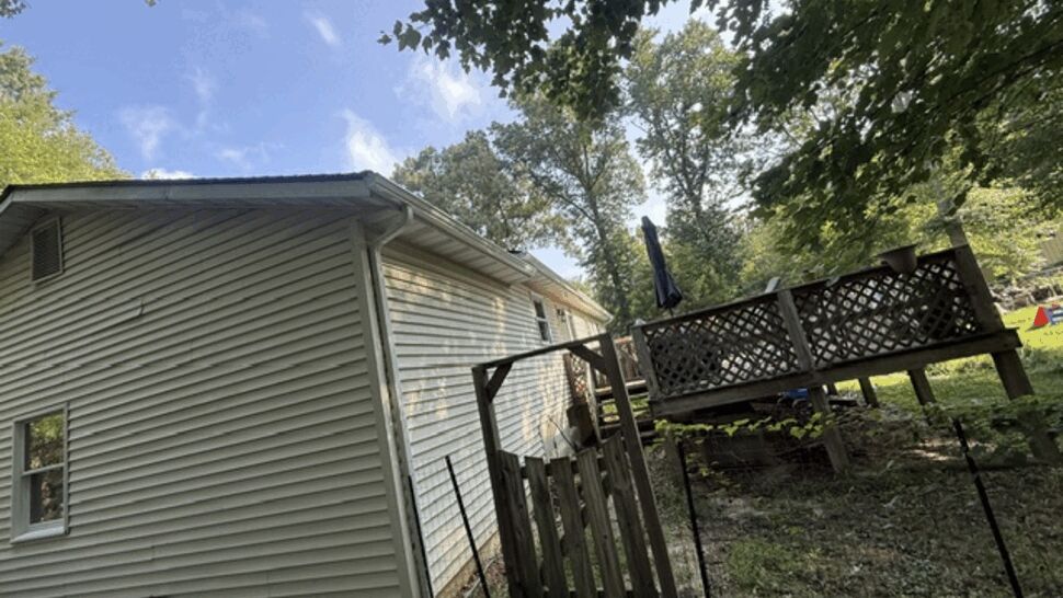 Side view of house showing vinyl siding, gutter, and a raised wooden deck.