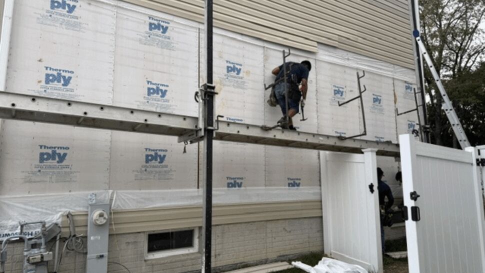 Crew on scaffold installing house wrap and siding panels.