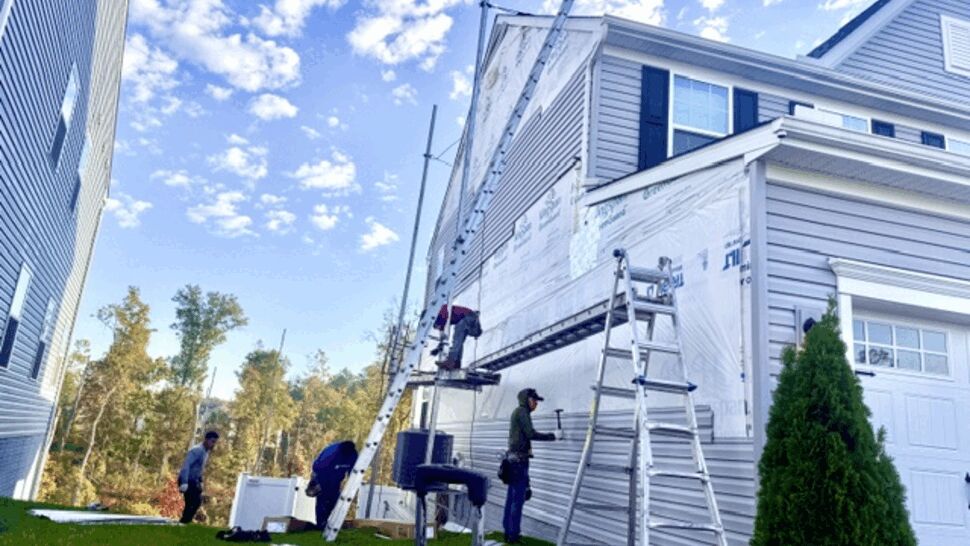 Siding crew working on a home exterior beside ladders and scaffolding