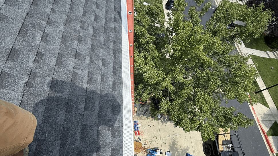 Steep gray shingled roof overlooking a residential street and parked cars.