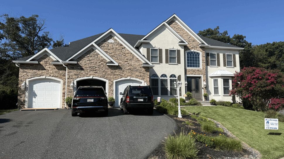 Two-story home with dark shingle roof, stone facade, and three-car garage.