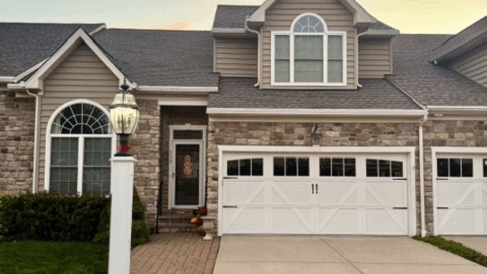 Two-story stone and siding home with dark shingle roof and white garage doors