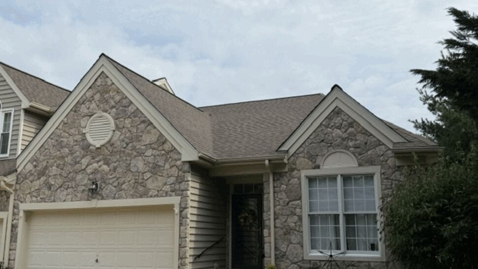 Front of stone-faced home with garage and brown roof.