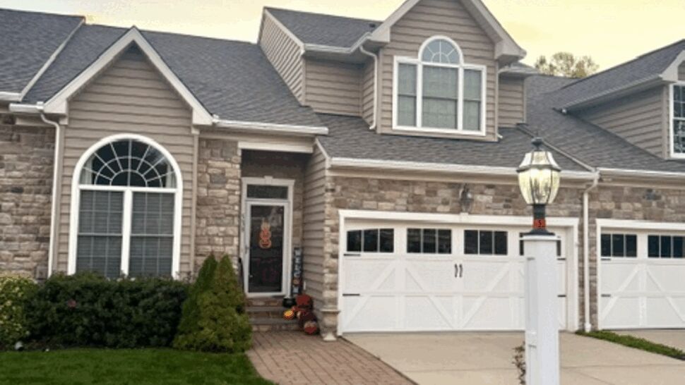 Suburban home with gray roof, stone facade, siding, and landscaped lawn