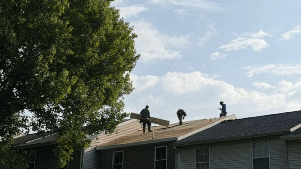 Three roofers carrying and installing roof sheathing on a townhouse roof.