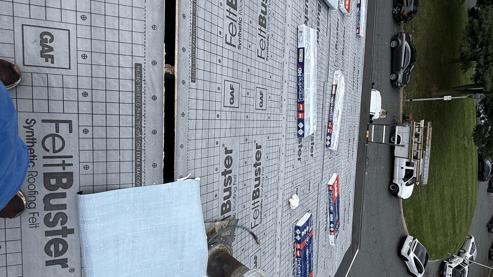 Roof covered in synthetic FeltBuster underlayment with bundles of shingles staged.