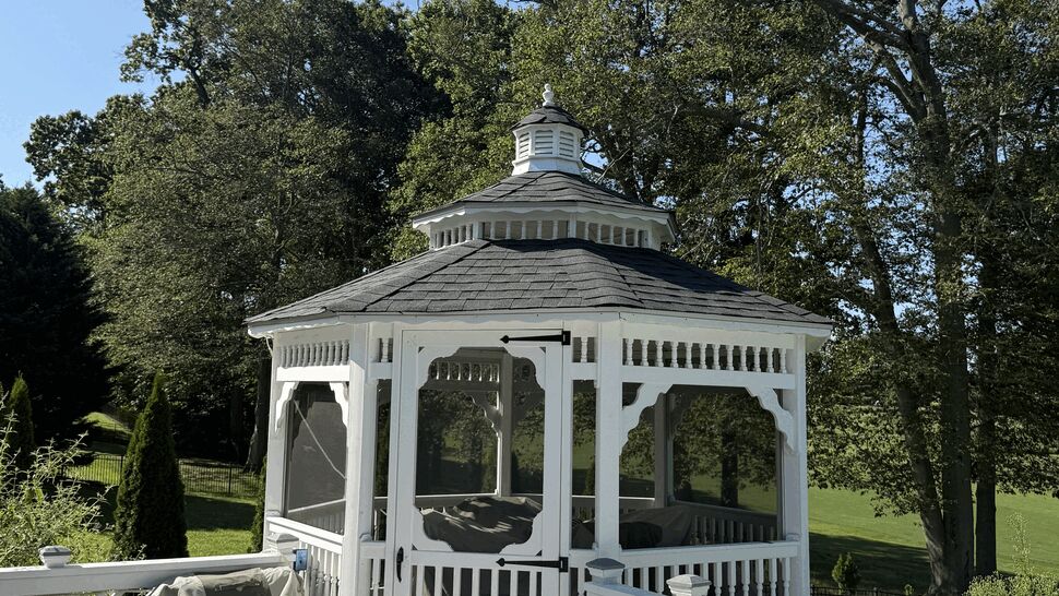 White wooden gazebo with an octagonal shingled roof surrounded by trees.