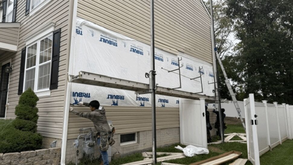 Worker adjusting downspout near utility meter with siding materials on ground.