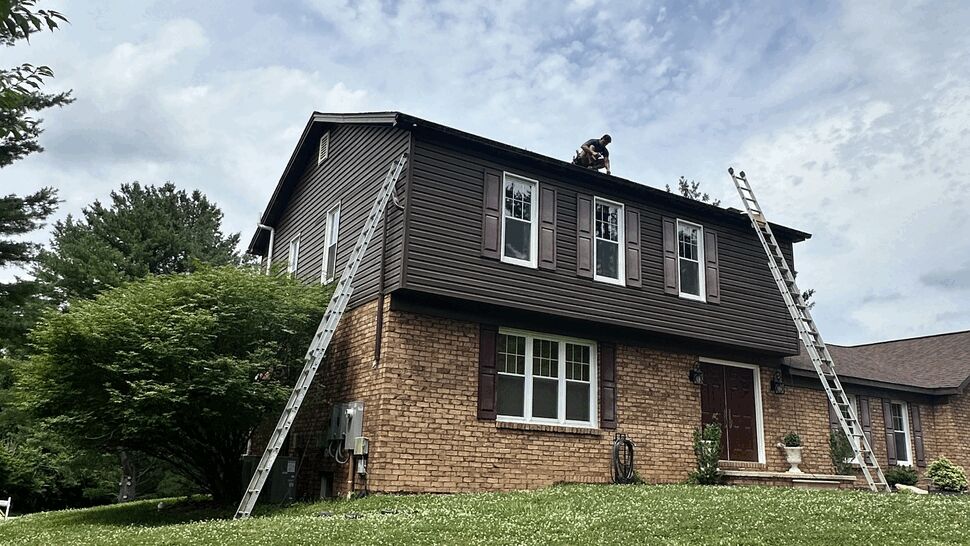 Contractors on ladders working on upper roof of brick home
