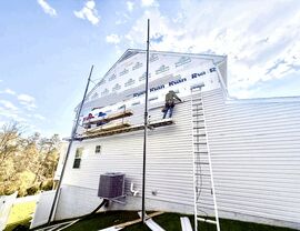 Workers installing siding panels on the rear wall of a two-story home