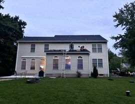 Back of house at dusk with workers on a lower roof and a ladder