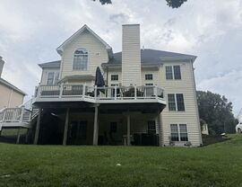 Rear of light-colored home with elevated deck and vinyl siding.