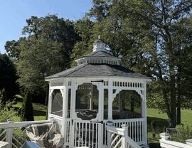 White wooden gazebo with an octagonal shingled roof surrounded by trees.