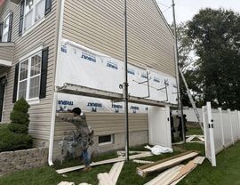 Worker adjusting downspout near utility meter with siding materials on ground.